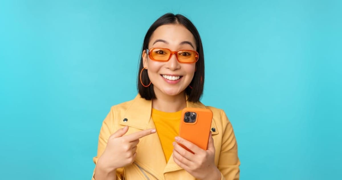 Person in sunglasses pointing at an orange smartphone