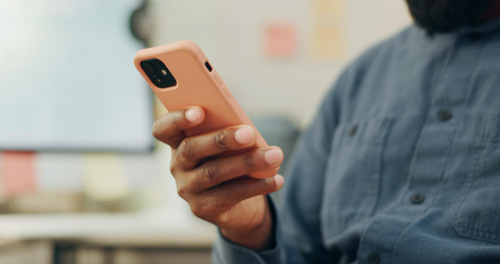 A hand holding a phone in an orange case