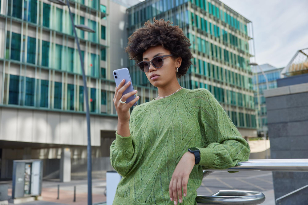 A woman in a green sweater checking her phone outside an office building