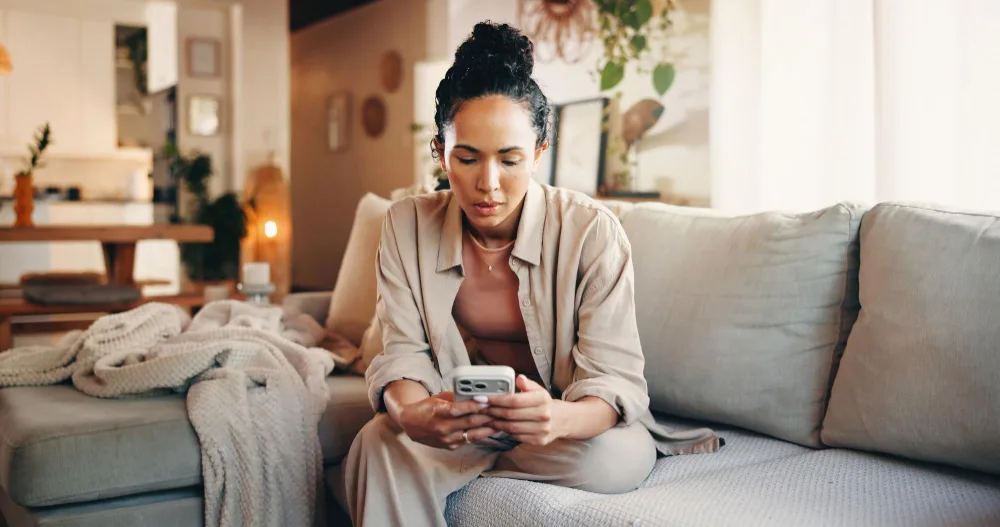 A woman sitting on a sofa at home reading something on her phone