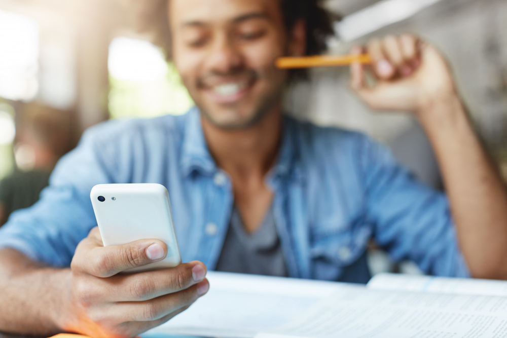 A man at a desk holding a phone, smiling, pencil in hand