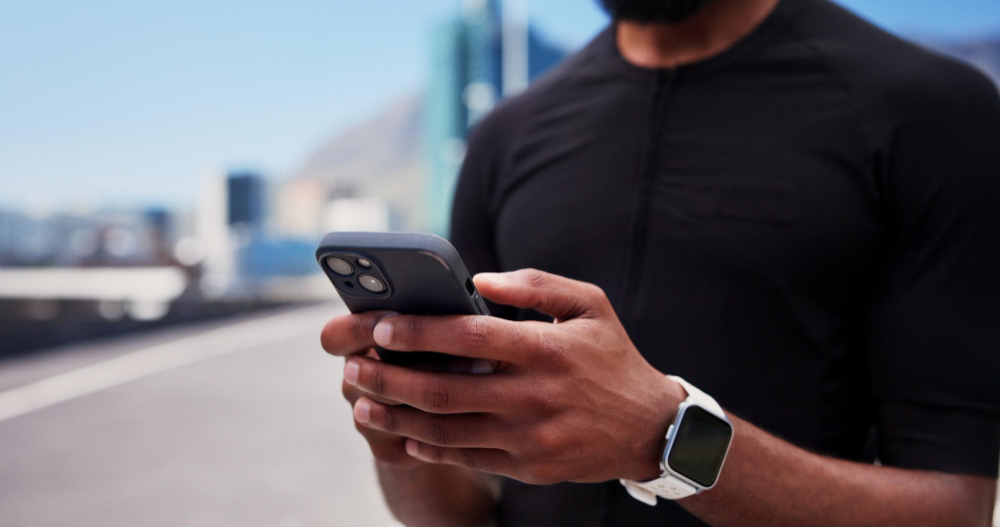 A man in a black shirt using his phone, wearing a smartwatch