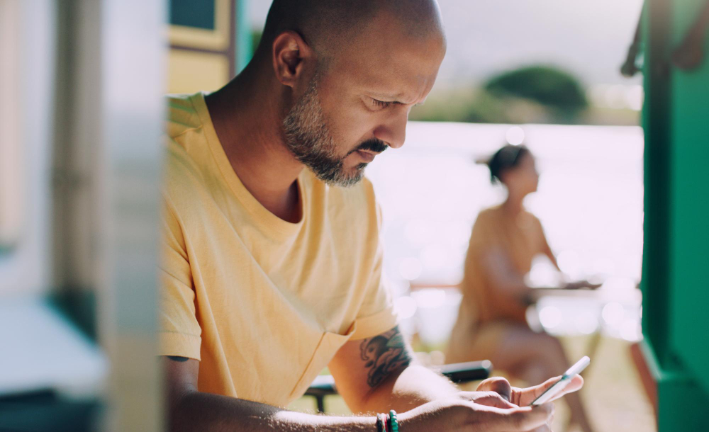 A man frowning at his phone on a sunlit balcony