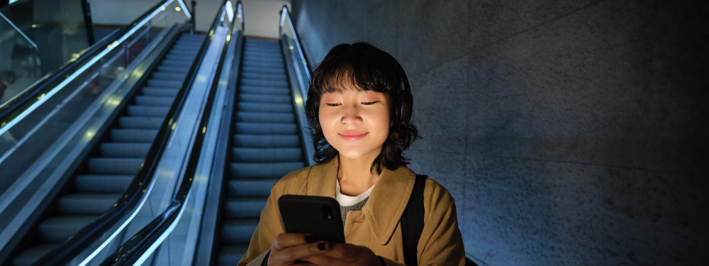 A woman smiling at her phone at the bottom of a subway escalator