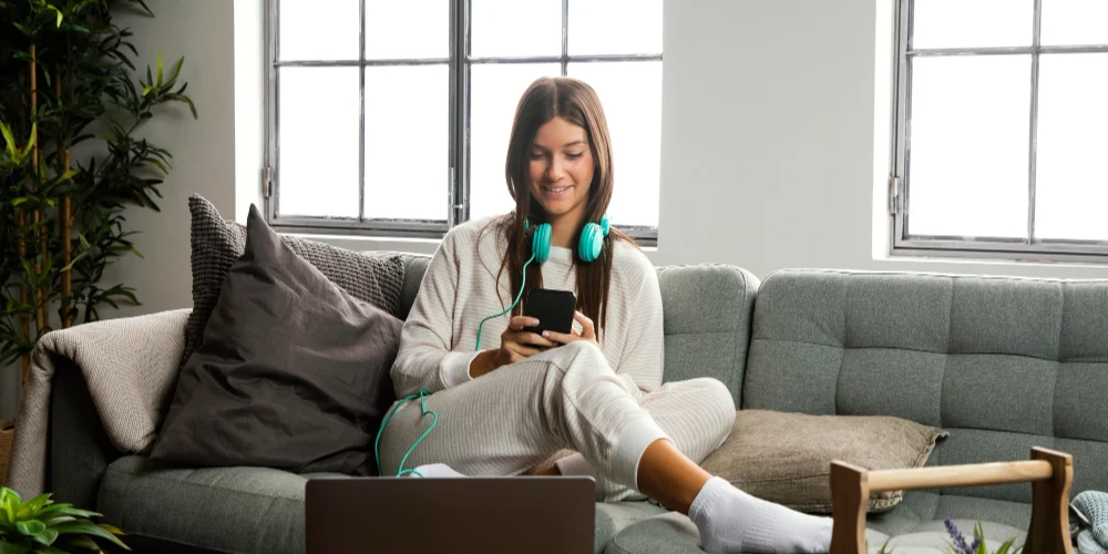 A woman uses her phone at home beside a laptop