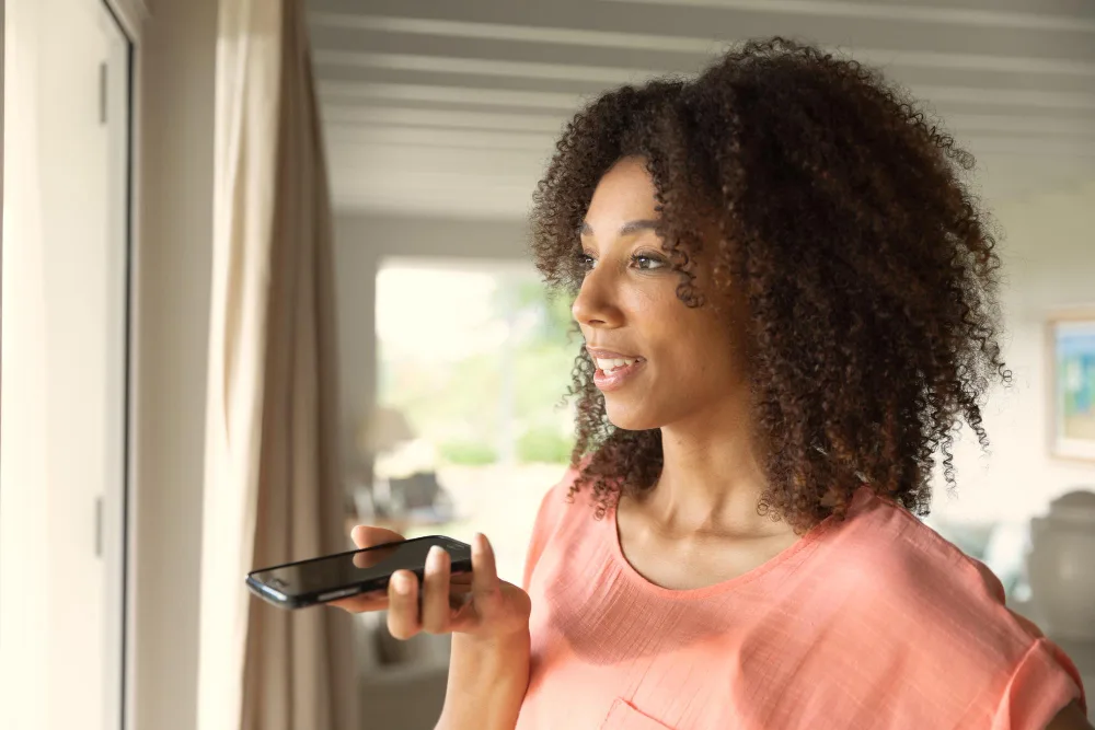 A woman speaking into her phone by a window at home