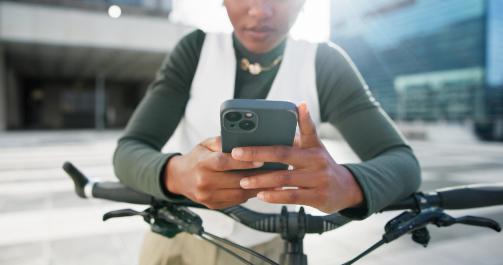A woman leaning on her bicycle, checking her phone