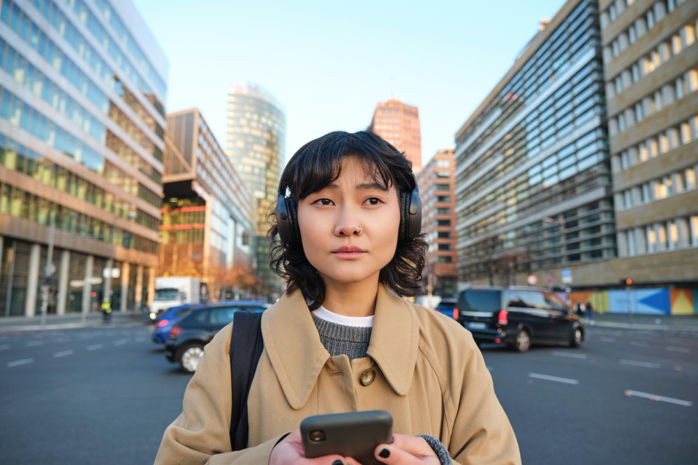 A woman in headphones holding her phone at a city intersection