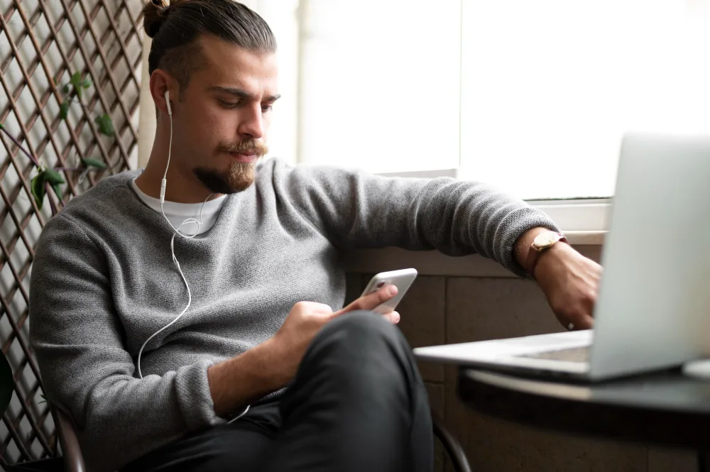 A man using his phone and laptop with earphones in
