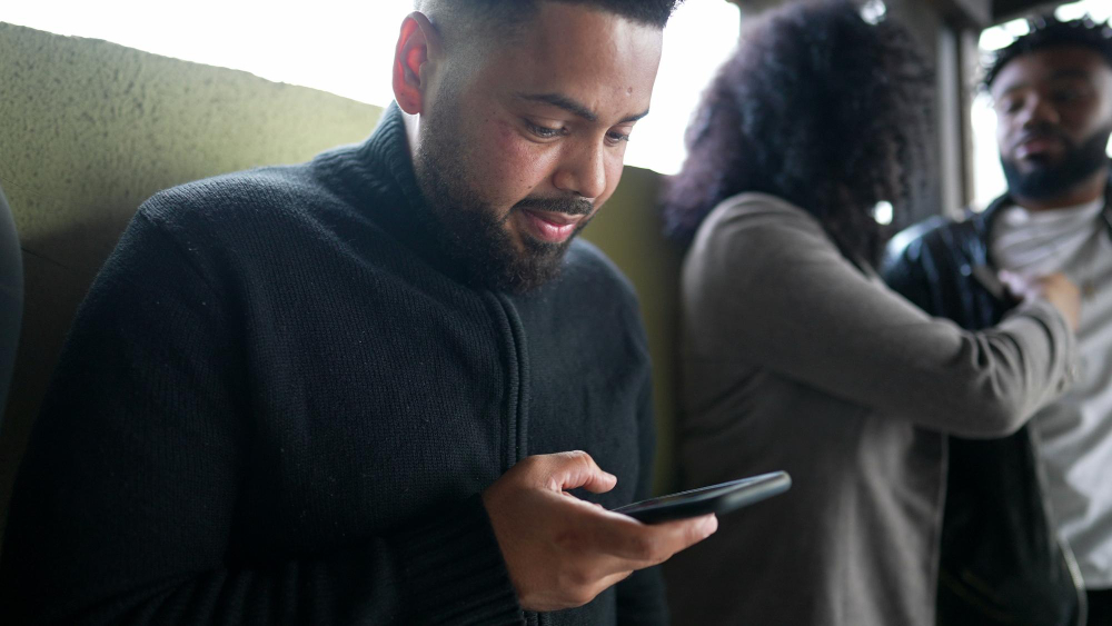 A man checking his phone while standing on a busy train