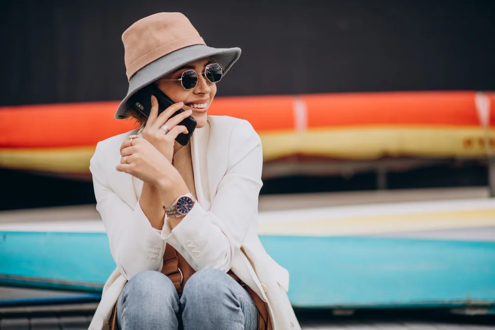 A woman in a sun hat taking a call beside boats at a marina