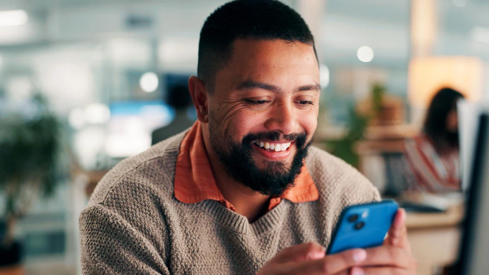 A man smiling at his phone in an open-plan office