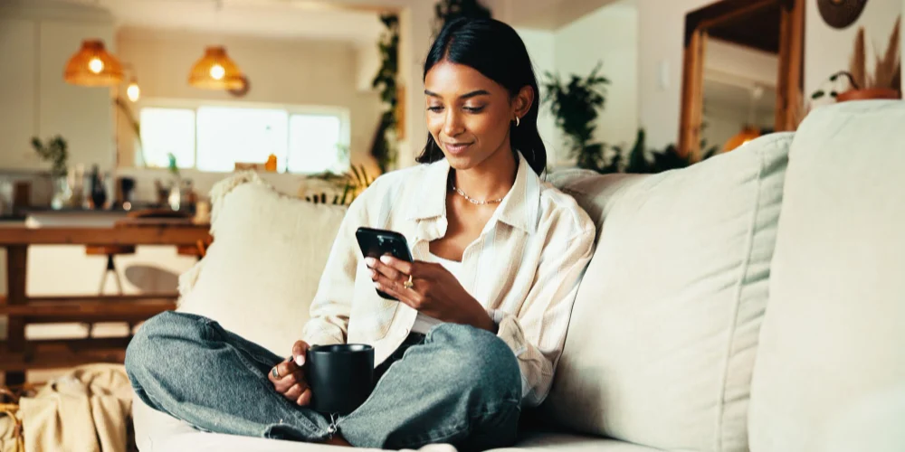 A woman uses her phone on a couch with a coffee
