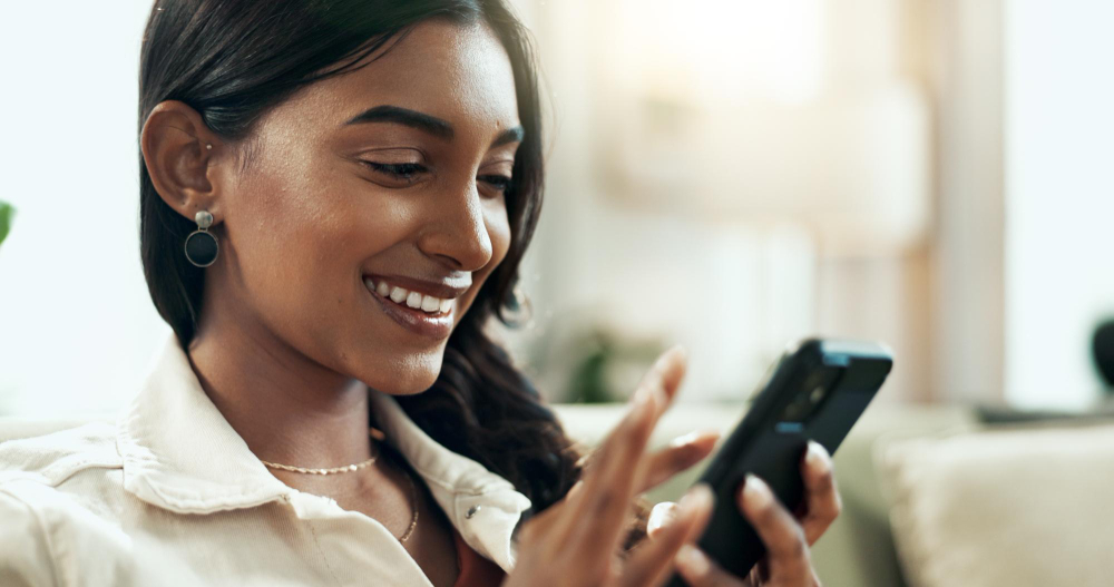 A woman sitting on a sofa, smiling at her phone