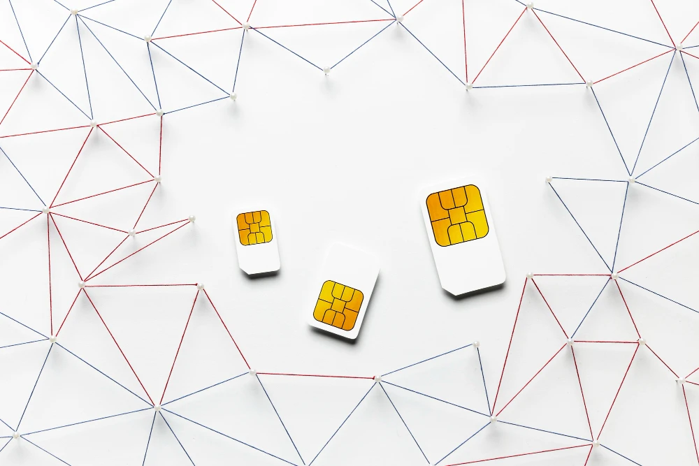 Three physical SIM cards on a white surface surrounded by a network of threads and pins